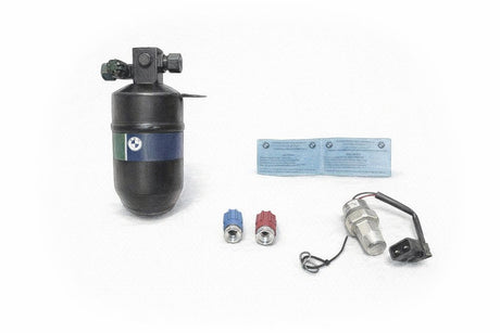 A BMW E30 R-134a conversion kit laid out on a bench with the new receiver/drier, R-134a service-port adapters, pressure switch, and conversion label.