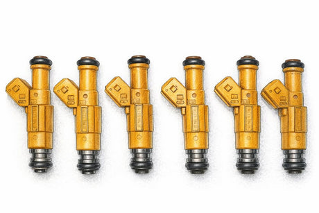 Six BMW M20 fuel injectors lined up in a row on a clean white bench, cleaned and resealed.